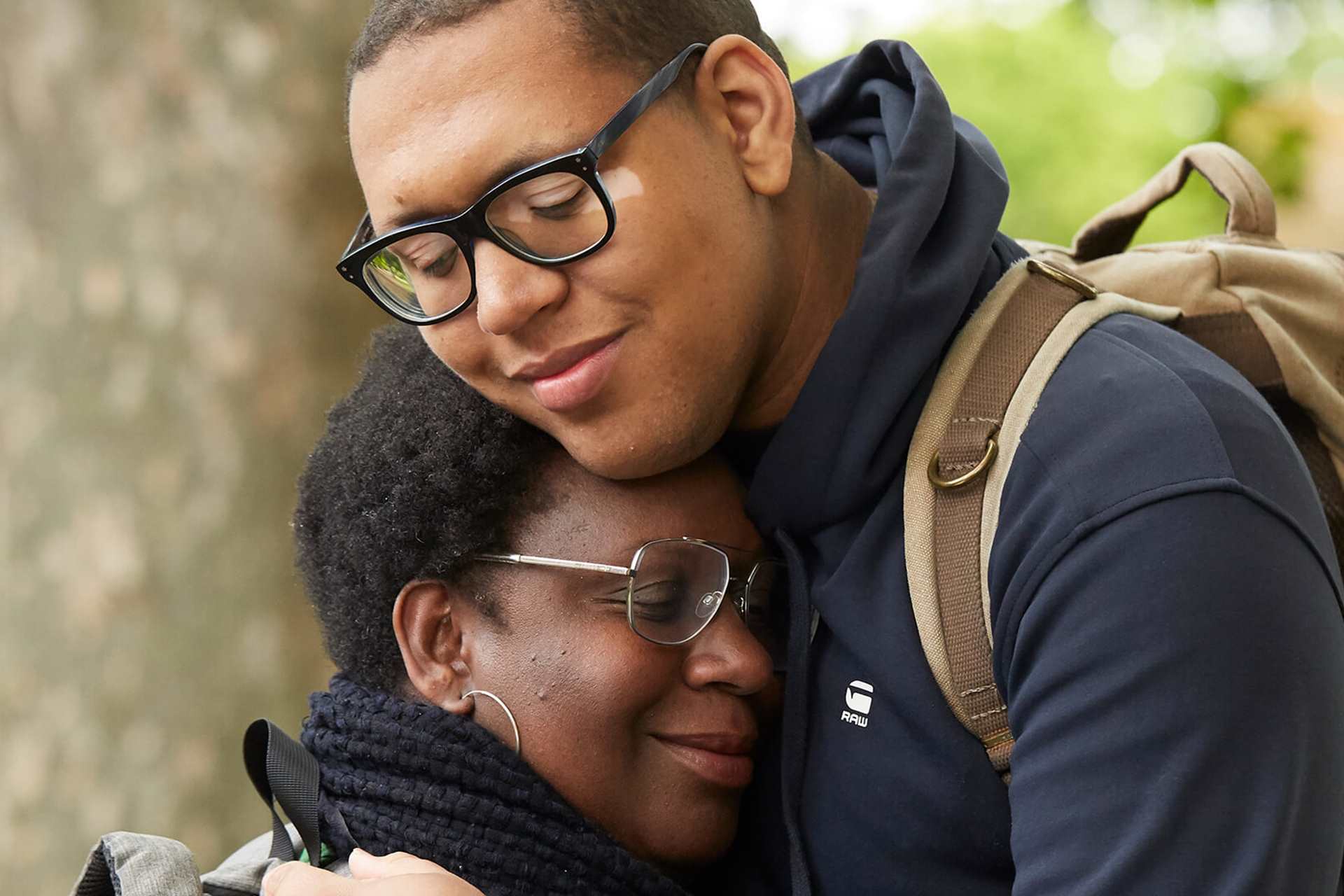 A mother and son smiling hugging in a park by a tree