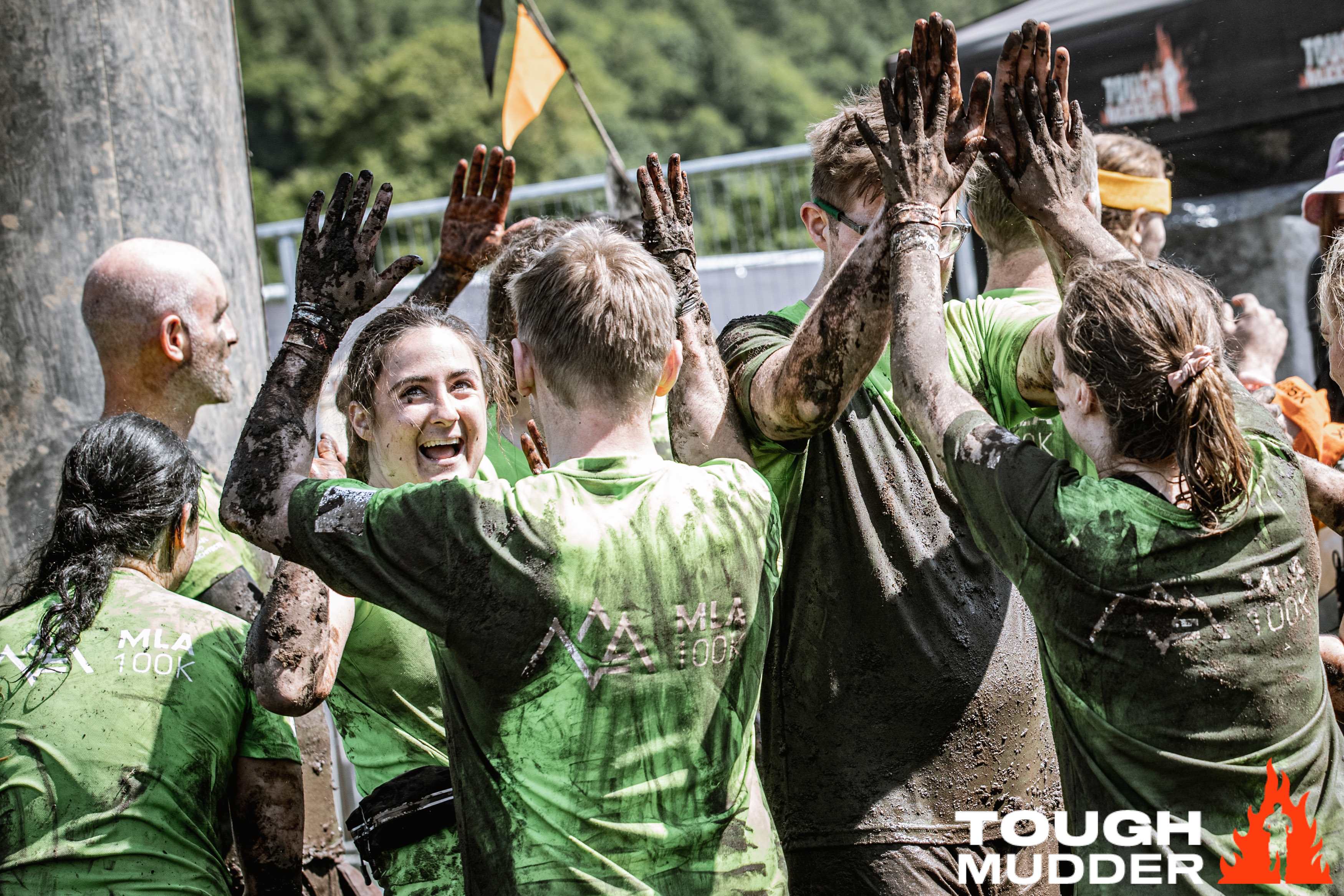 Tough Mudder participants cheering and hi-fiving, covered in mud