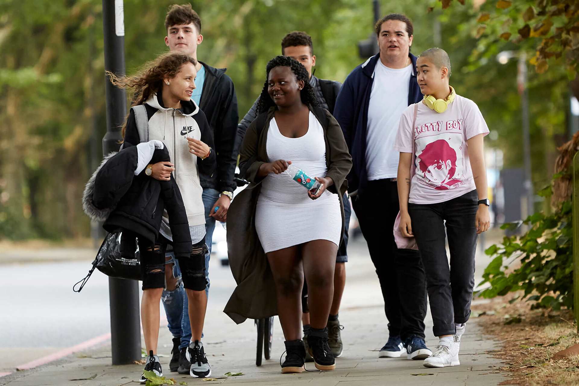 Six young people chatting as they walk through a park together.