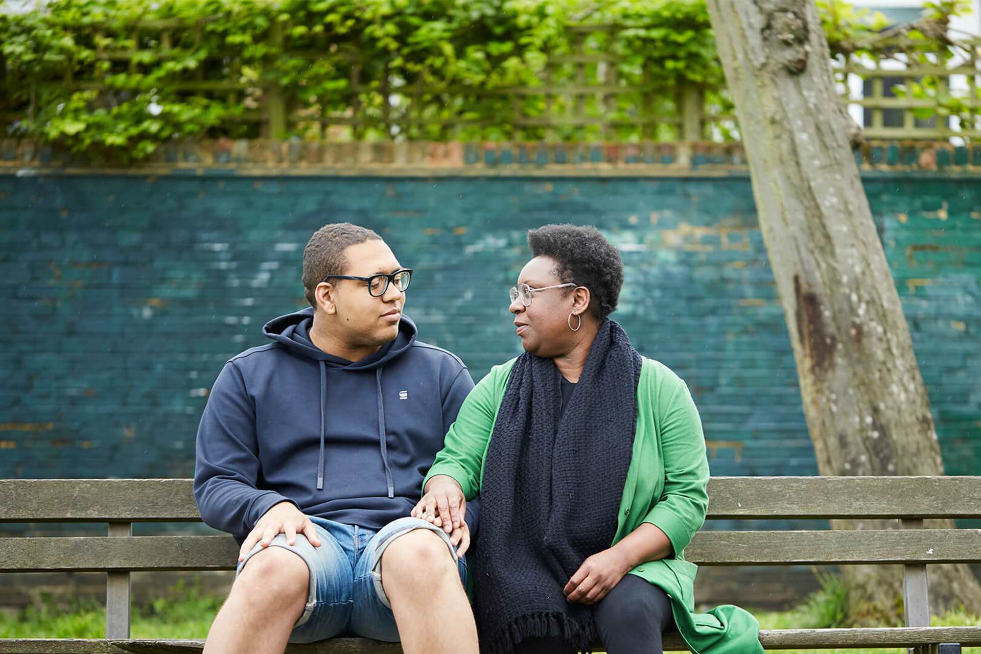A mother and son holding hands on a bench looking at each other