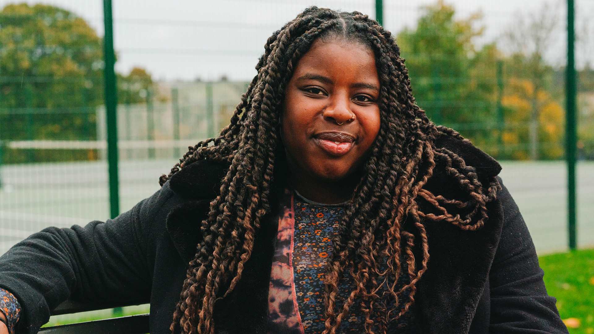 A young Black woman sitting on a bench in the park. She is smiling.