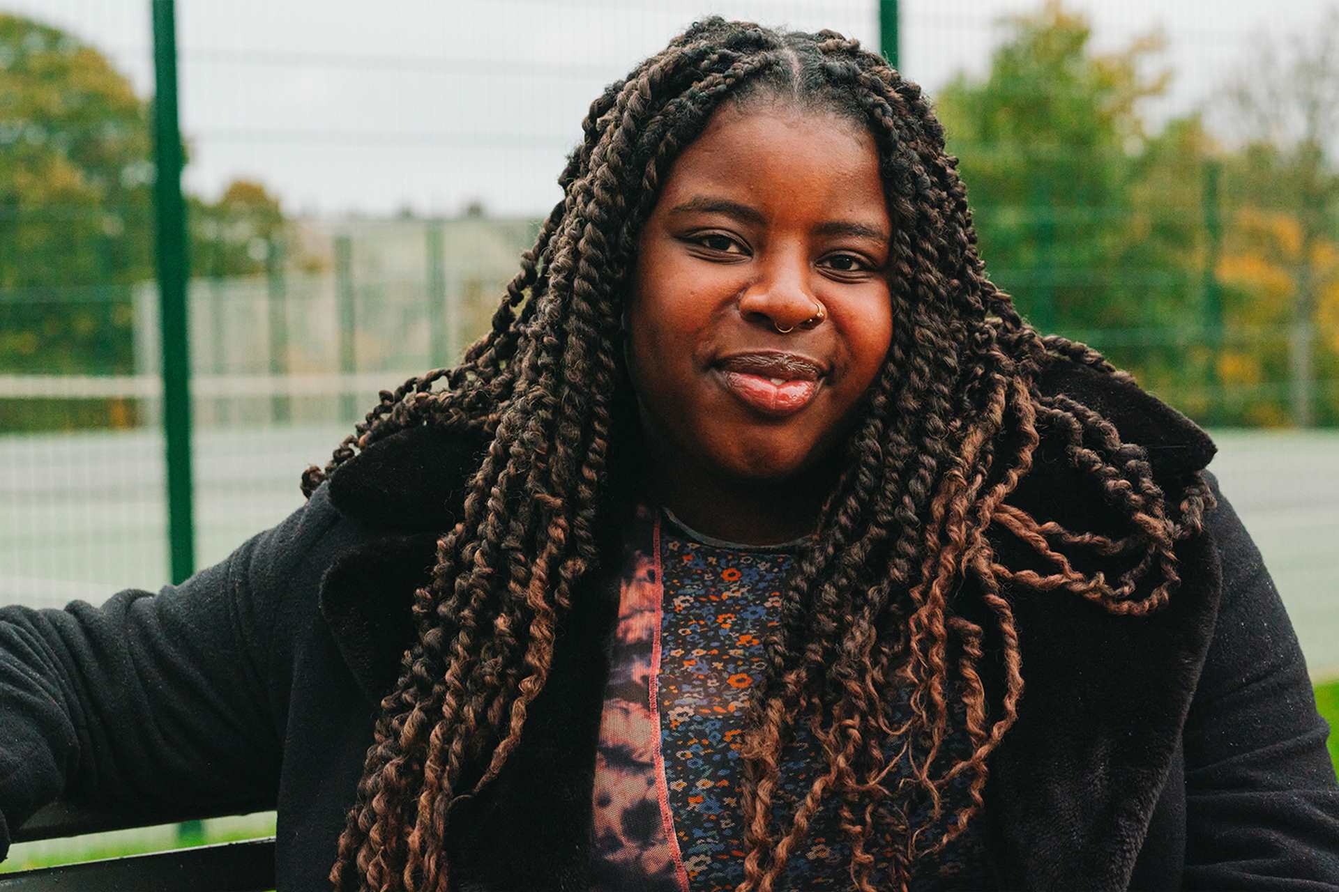A young Black woman sitting on a bench in the park. She is smiling.