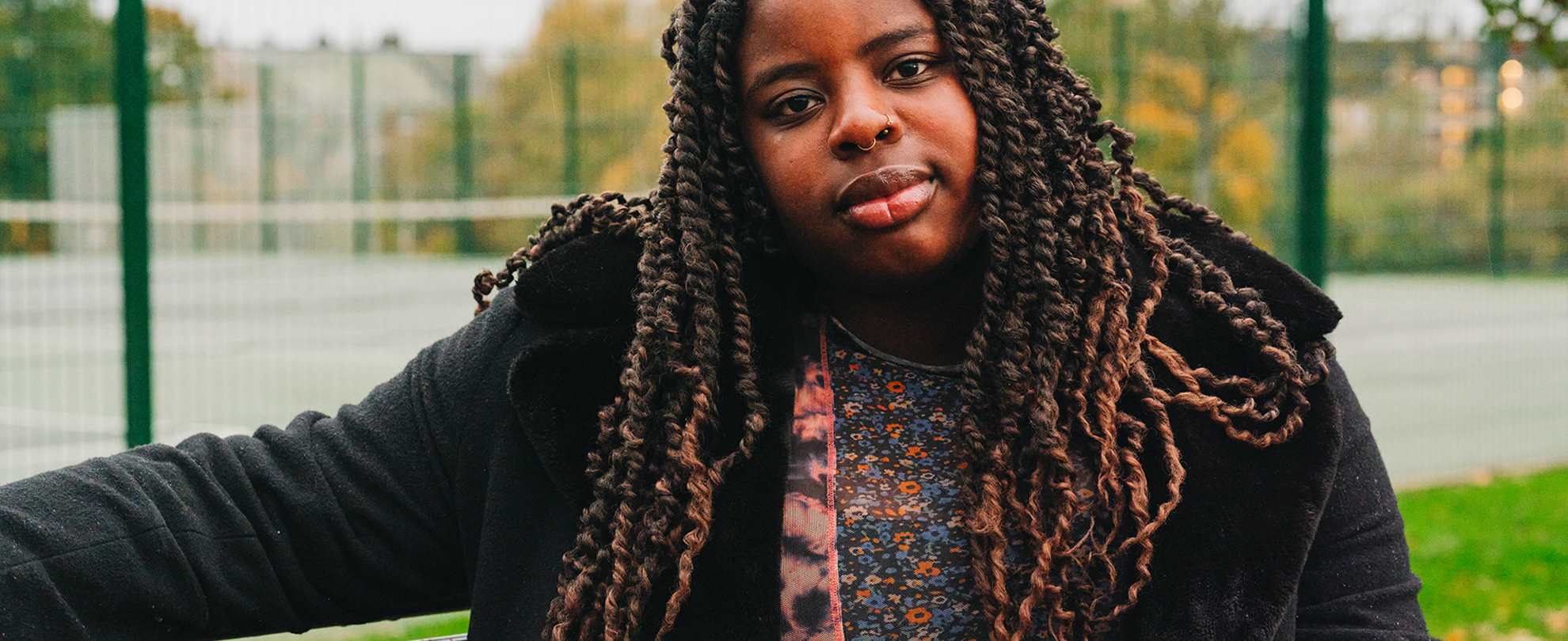 A young Black woman sitting on a bench in the park.