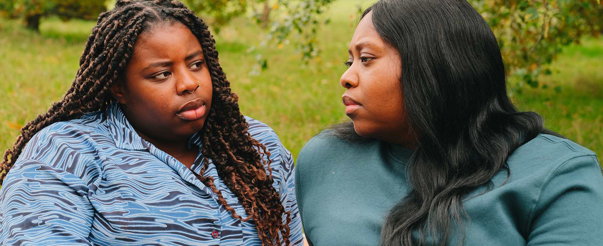 A young Black woman talking about something serious with an older Black woman in the park.