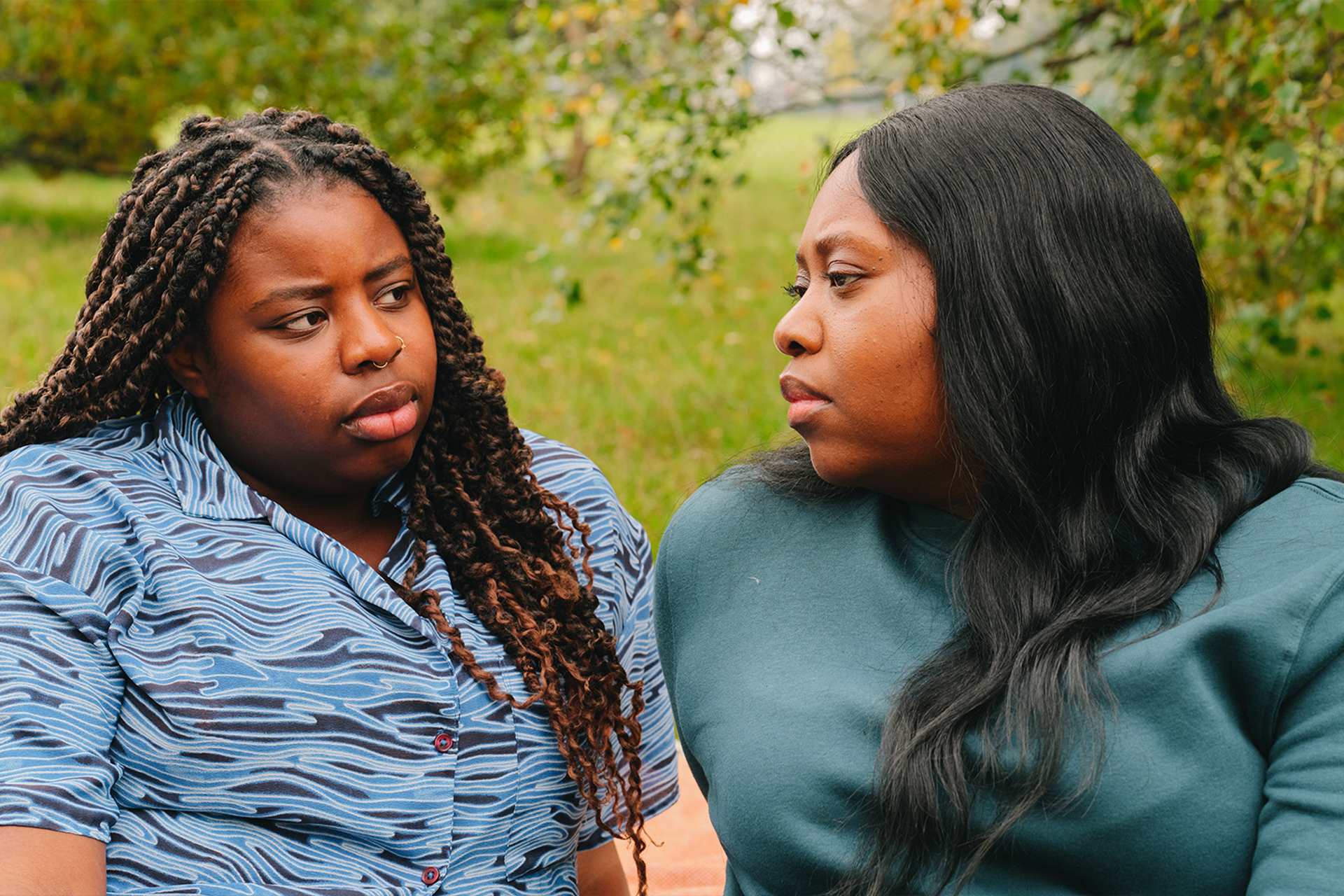 A young Black woman talking about something serious with an older Black woman in the park.