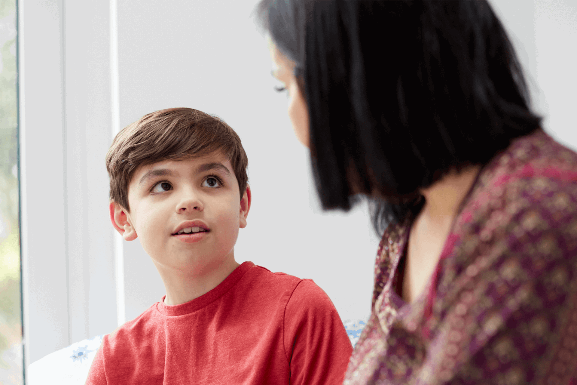 A mother and her young son look at each other near a window