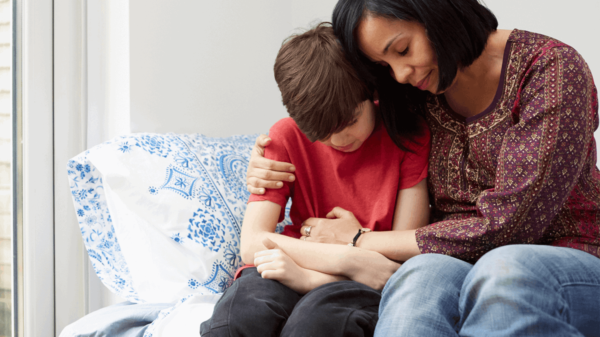 A mother comforting her young son at home in a conservatory 