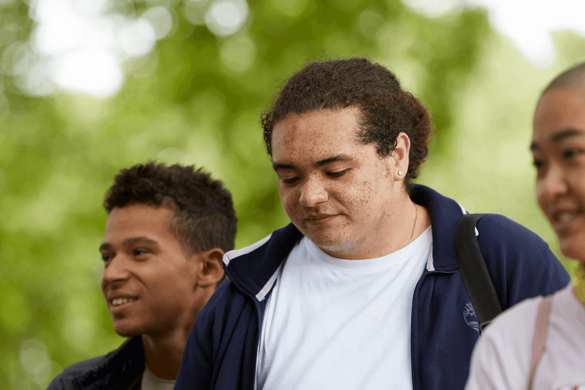 Three young people walking together through a park. Two of them are smiling while a boy in the centre looks worried.