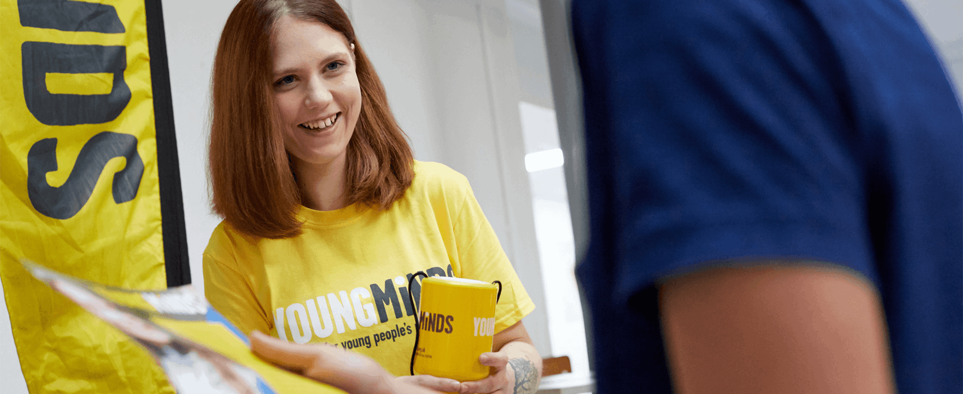 a YoungMinds volunteer wearing yellow YoungMinds shirt smiling in a fundraising event