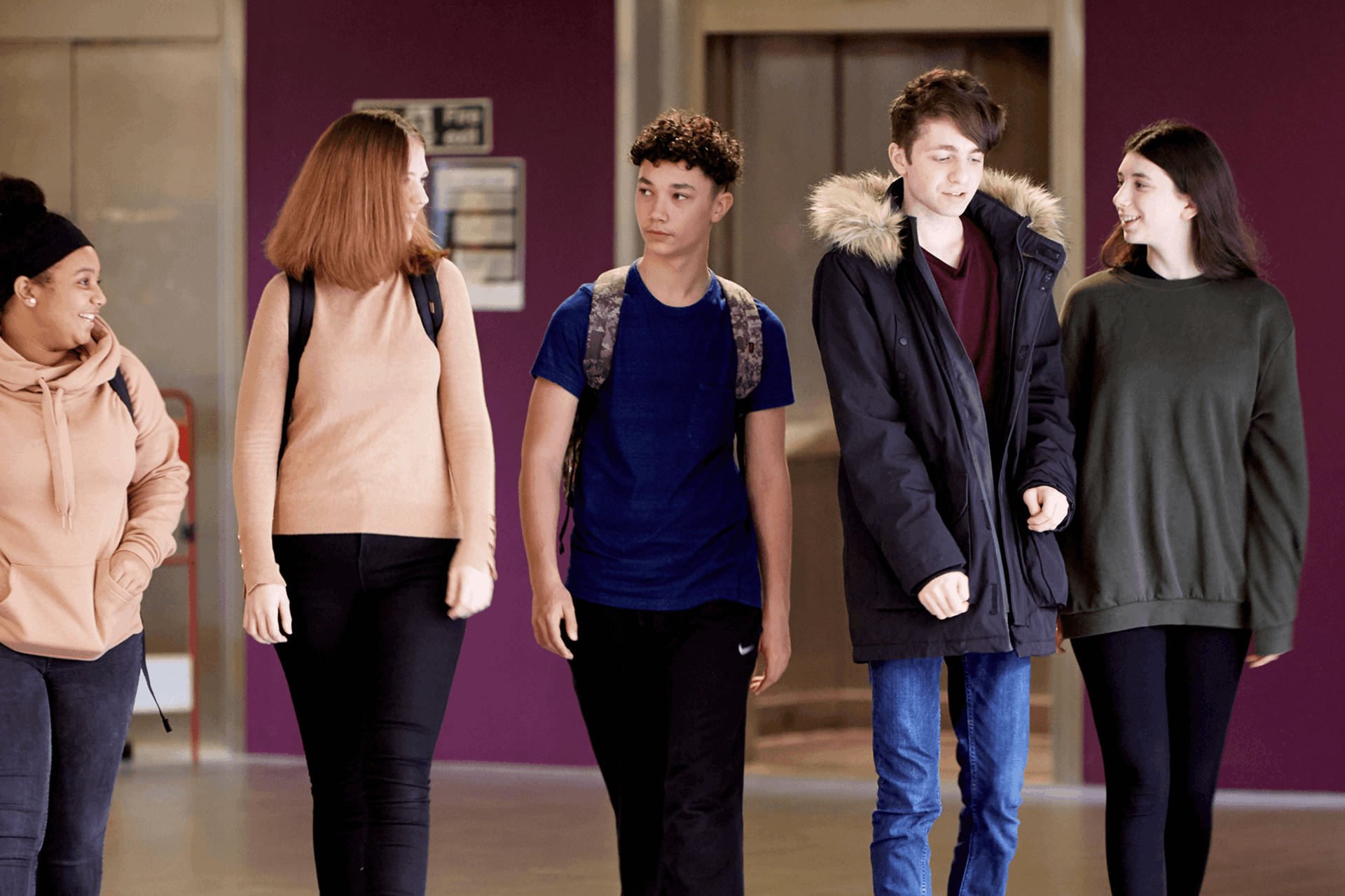 wide shot of five students wearing backpacks walking and talking inside the campus