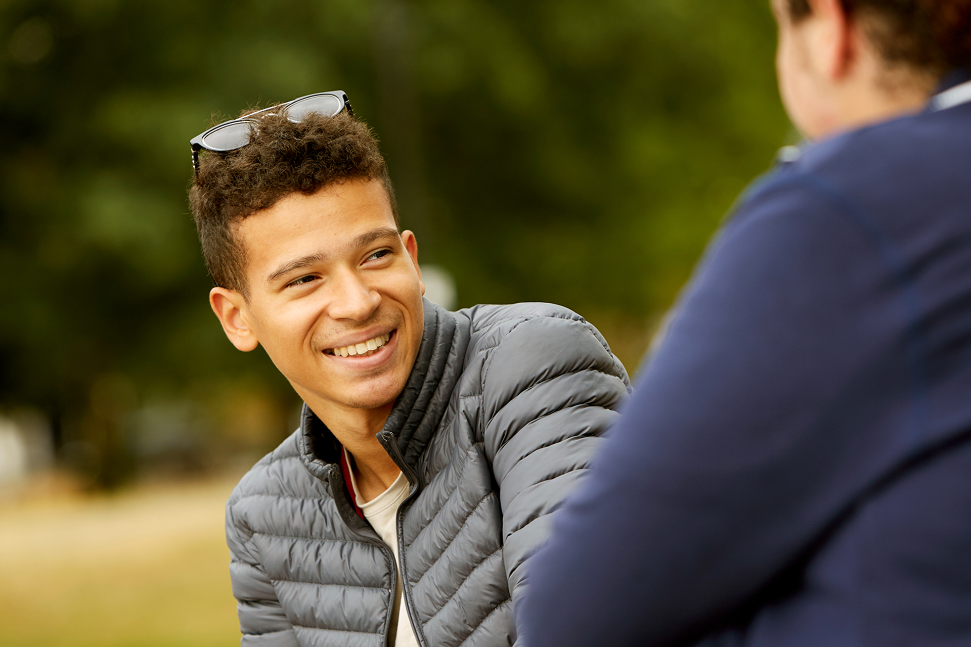 A boy smiling at his friend in the park.