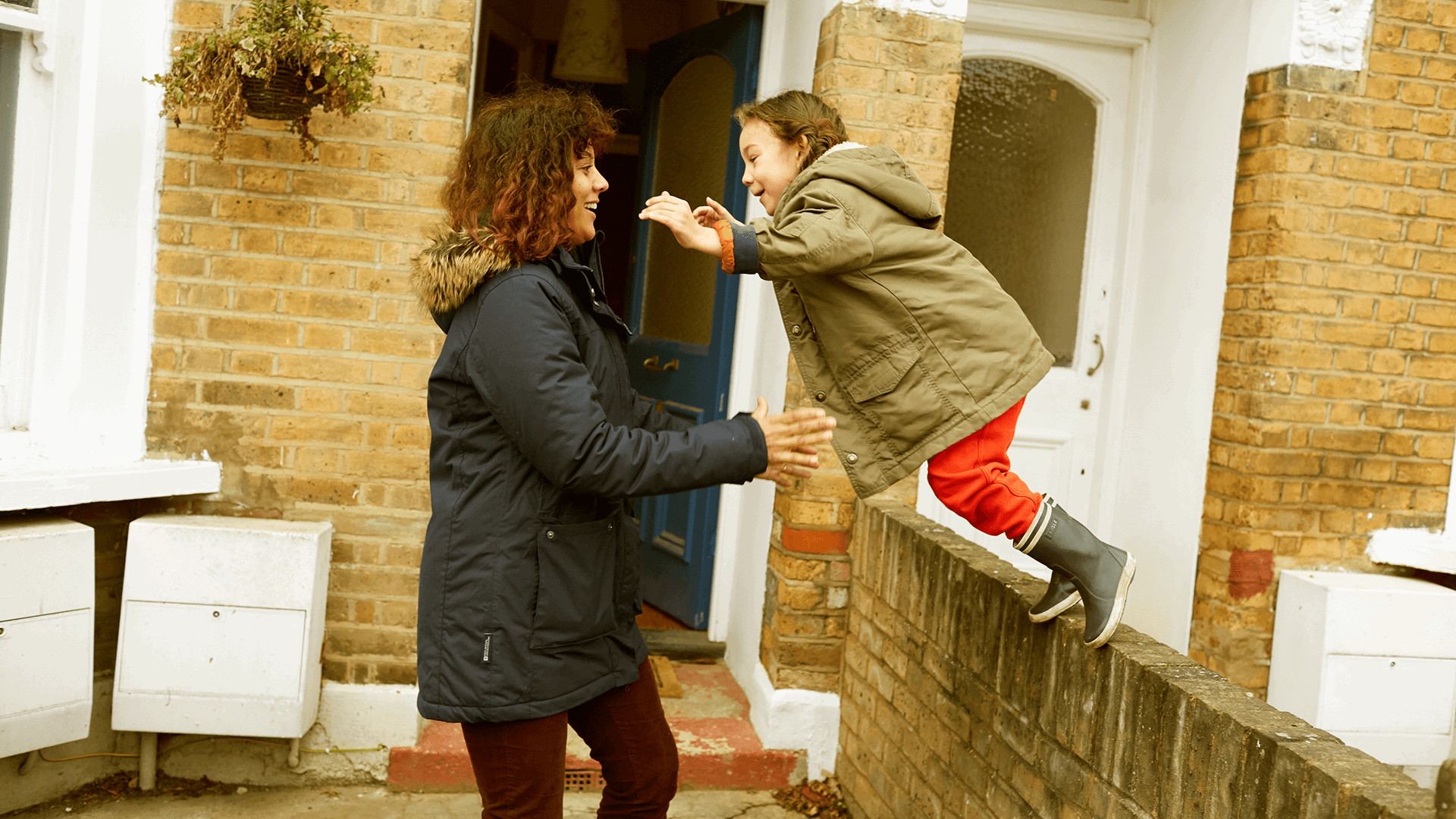 A child jumping off a wall and her mum is ready to catch her.