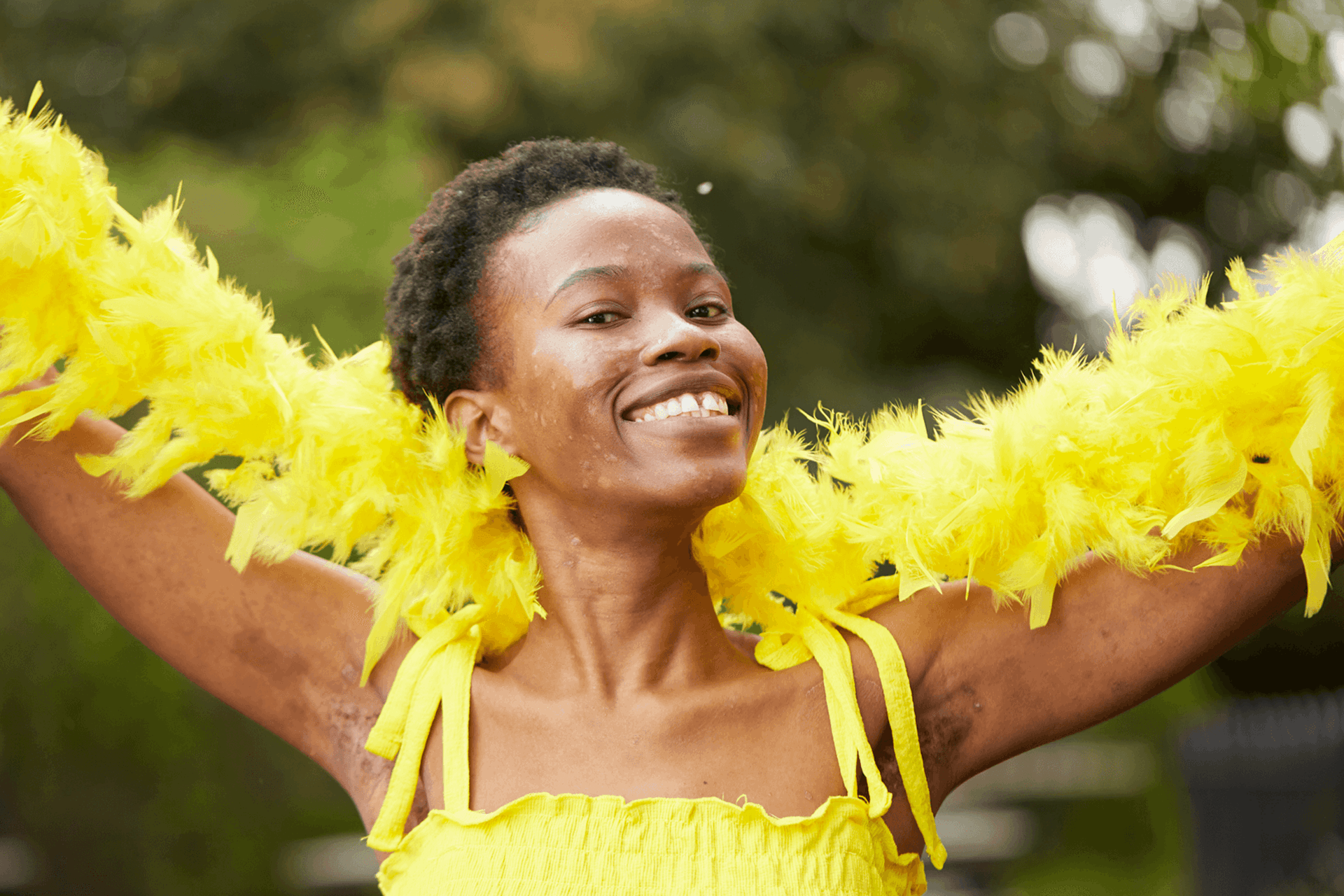 medium shot of a fundraising ambassador wearing yellow dress and yellow feather scarf smiling at the camera