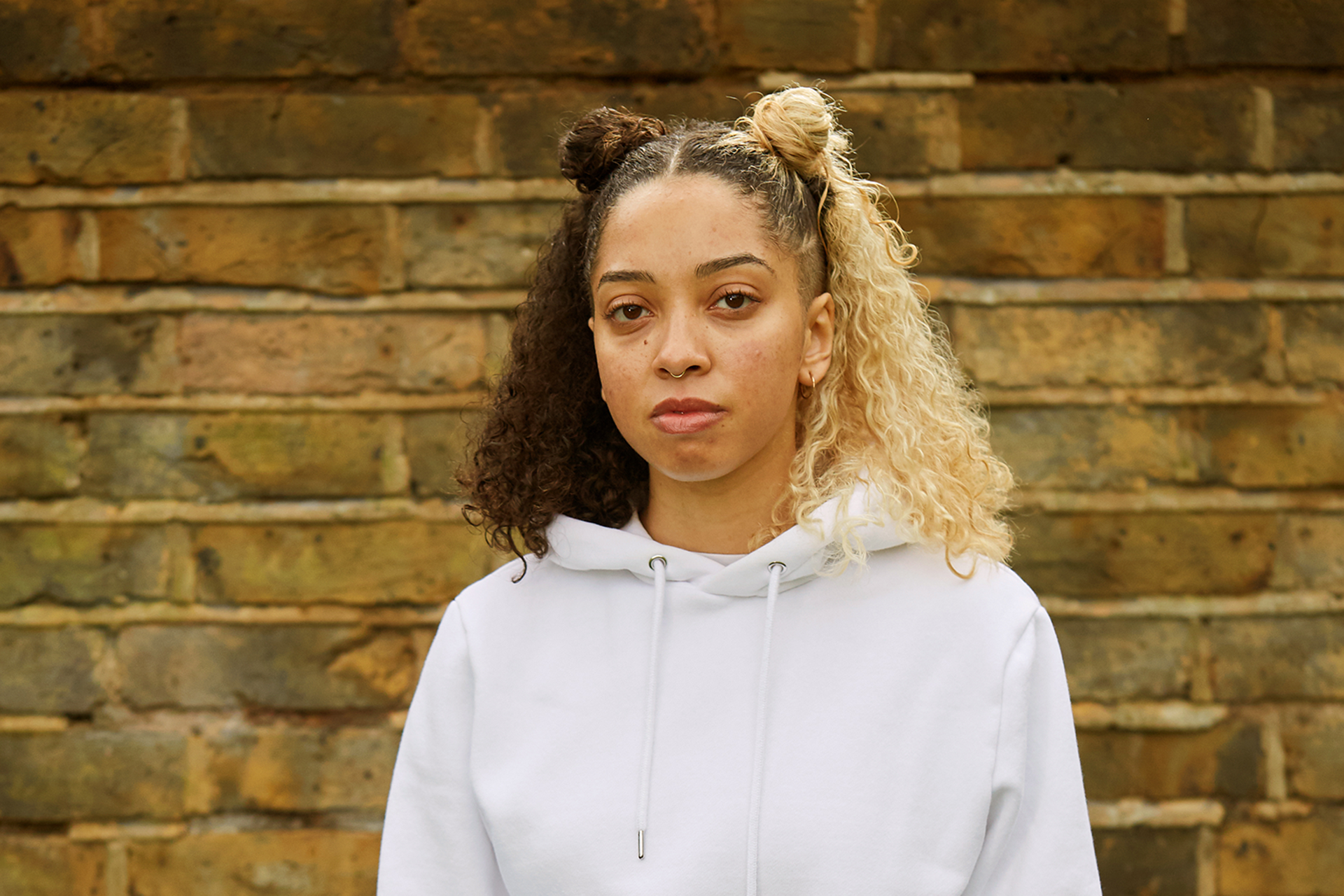 A girl staring at the camera in front of a brick wall.