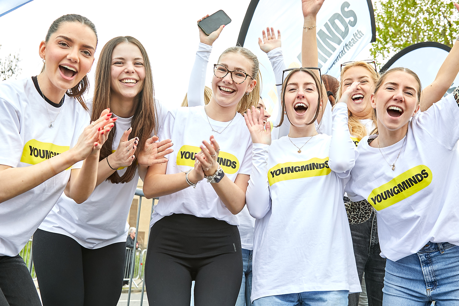 The YoungMinds fundraising team cheering with their hands in the air at the marathon. They are wearing YoungMinds t-shirts and have YoungMinds banners.