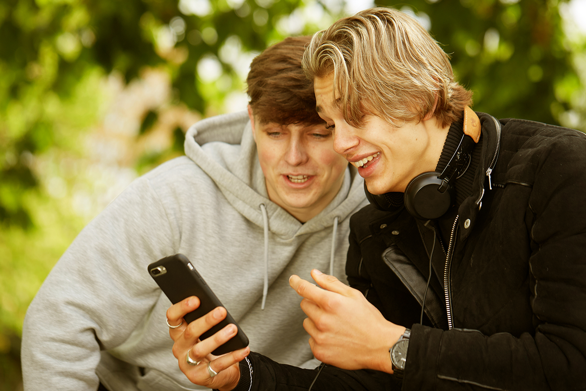 Two boys looking at a phone and smiling in the park.