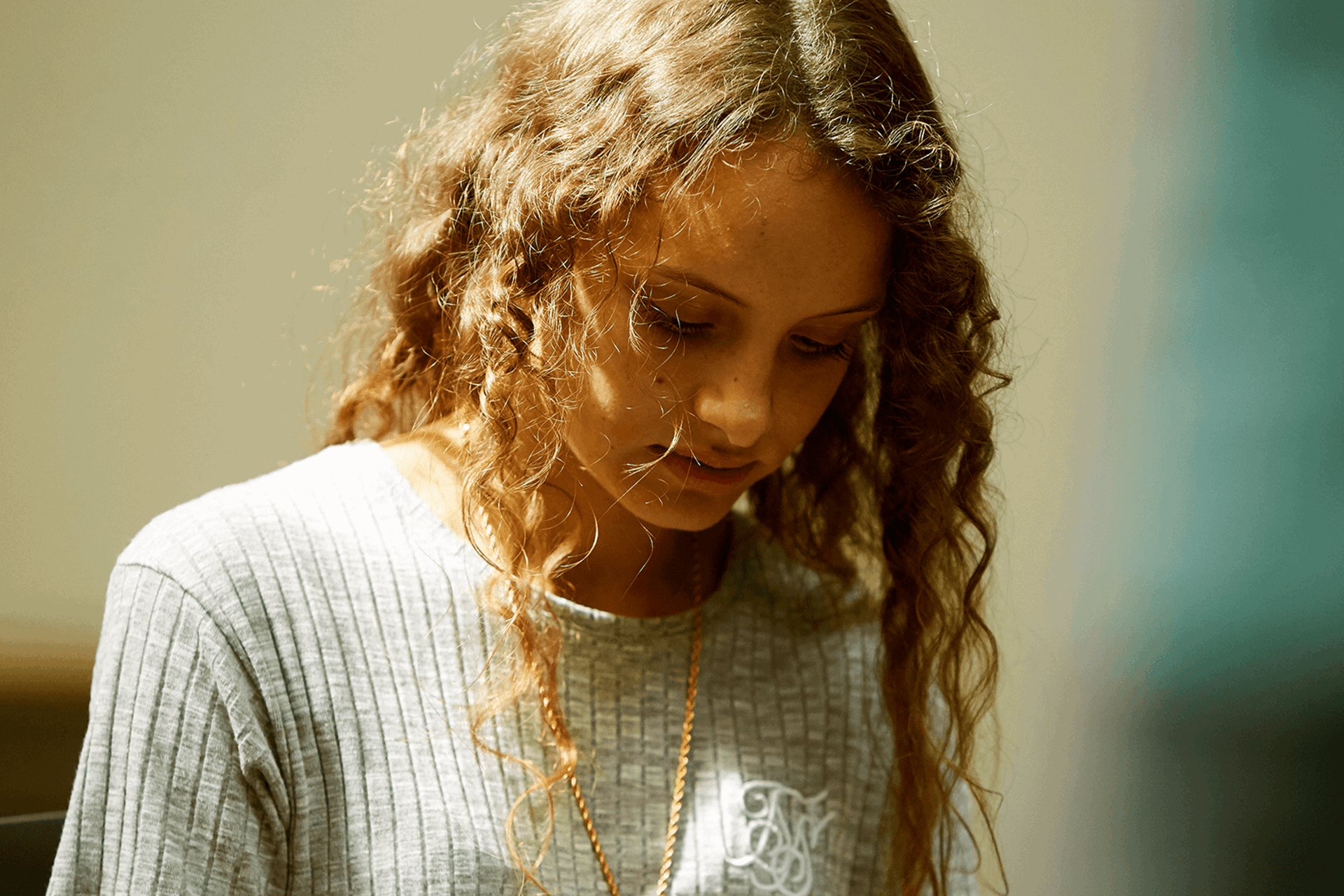 A young person alone and looking down at the ground.